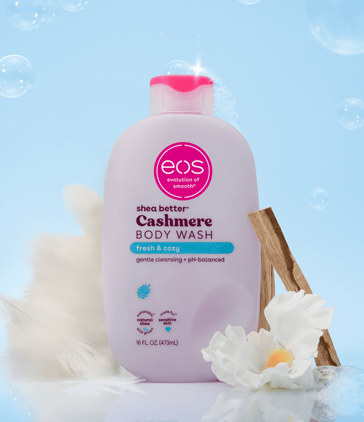 EOS Fresh & Cozy Body Wash 473ml with white flowers, soft fabric, wood accents and bubbles against a blue background