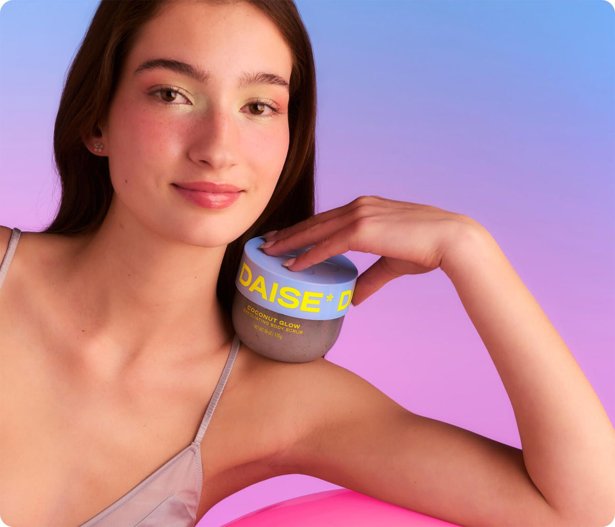 Daise Coconut Glow Exfoliating Body Scrub 510g held beside a model's shoulder