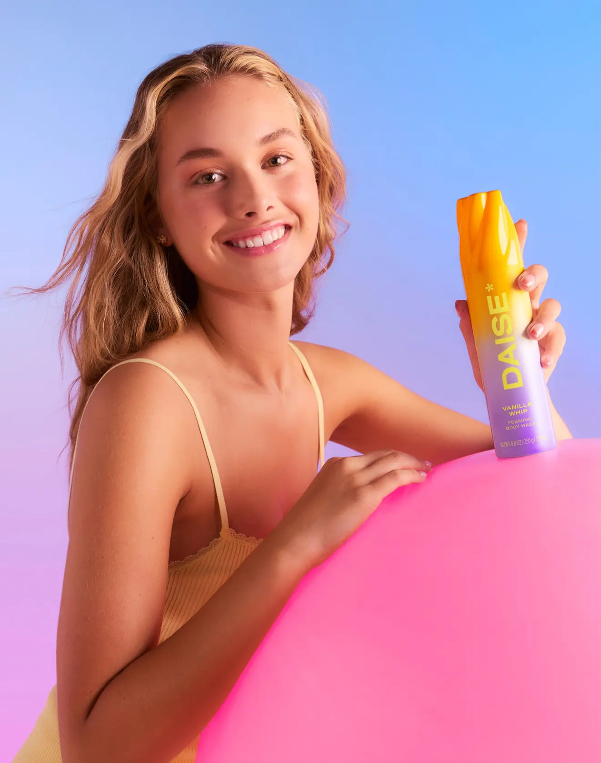 HAMYNAT model smiling while holding a DAISE Vanilla Whip foaming body wash in a vibrant yellow and purple ombre bottle.