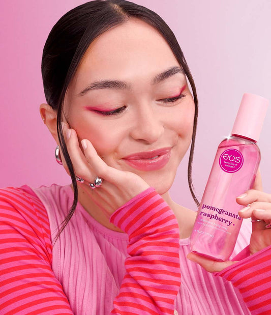 HAMYNAT model holding an eos pomegranate raspberry cashmere body mist with matching pink makeup against a pink background