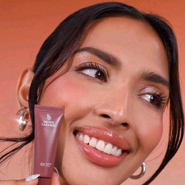 HAMYNAT model smiling while holding a brown eos Salted Caramel hydrating lip treatment tube with a glossy finish