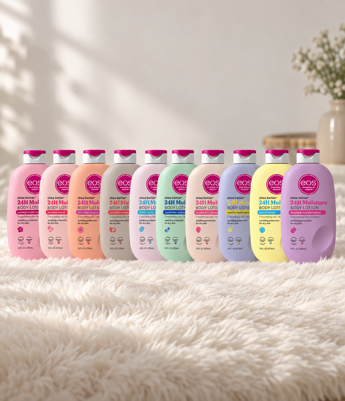 HAMYNAT collection of ten colourful eos Shea Better 24H moisture body lotion bottles arranged on a fluffy white rug.