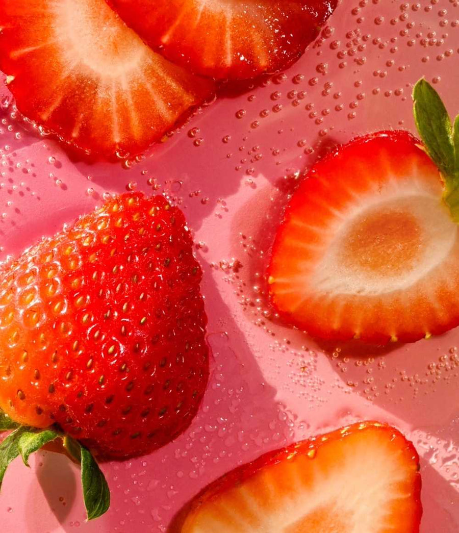 HAMYNAT eos Strawberry Sorbet organic lip balm represented by fresh sliced strawberries on a vibrant pink background