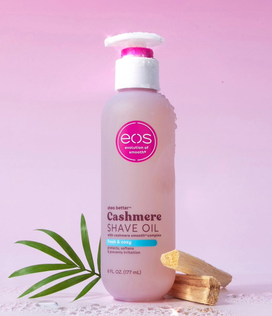 EOS Cashmere Shave Oil bottle with pump dispenser on a pink background with palm leaf and wood sticks