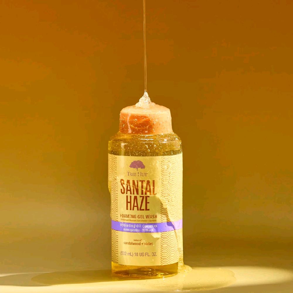 Tree Hut Santal Haze foaming gel wash bottle with golden liquid pouring over the top